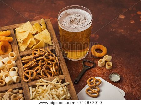Glass Of Craft Lager Beer And Opener With Box Of Snacks On Brown Kitchen Background. Pretzel,salty P