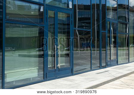 Diagonal View Of Modern Building Wall With Bif Glass Window And Door With Blue Frame. Street Reflect