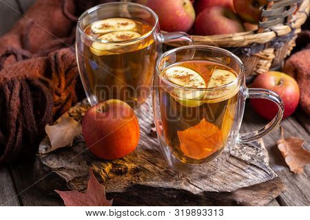 Two Cups Of Apple Cider With Apple Slices Sprinkled With Cinnamon On A Rustic Wooden Surface And Bas