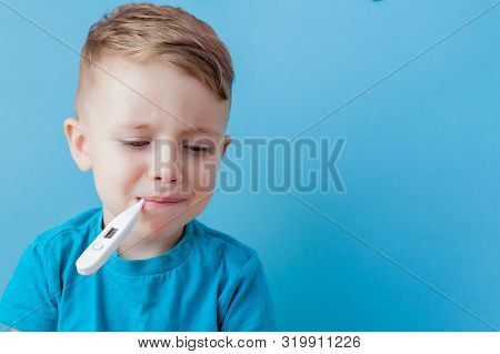 Ill Young Child With A Thermomether, Measuring The Height Of His Fever And Looking Into The Camera