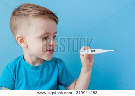 Ill Young Child With A Thermomether, Measuring The Height Of His Fever And Looking Into The Camera