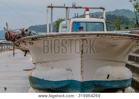 Closeup Of Fore Section Of Blue And White Fishing Boat On Concrete Pier On Rainy Morning.