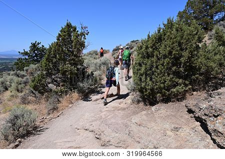 Hikers On Misery Ridge Trail In Smith Rock State Park Near Terrebonne, Oregon On A Cloudless Summer 