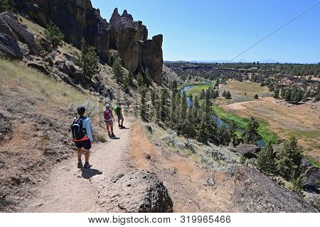 Hikers On Misery Ridge Trail In Smith Rock State Park Near Terrebonne, Oregon On A Cloudless Summer 