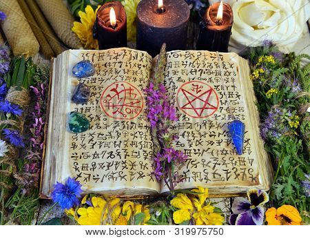 Witch Book With Spells And Magic Symbols, Black Candles, Reiki Crystals And Flowers. Esoteric, Occul