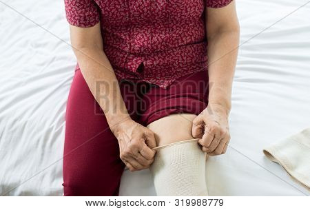 Senior Asian Woman Using Elastic Bandage With Leg,female Putting Bandage On Her Injured Knee
