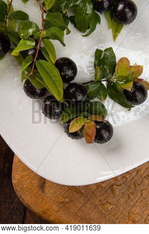 Jabuticaba, Jabuticabas In Detail Inside A White Plate With Branches And Leaves On Rustic Wood, Sele