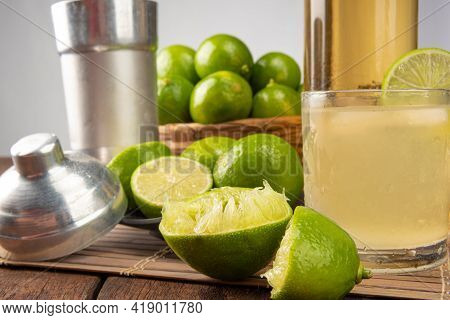 Brazilian Drink Caipirinha, Glass Of Caipirinha, Bottle Of Cachaça, Cocktail Shaker And Lemons On Wo
