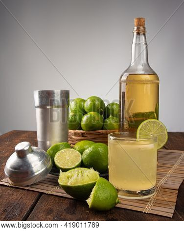 Brazilian Drink Caipirinha, Glass Of Caipirinha, Bottle Of Cachaça, Cocktail Shaker And Lemons On Wo