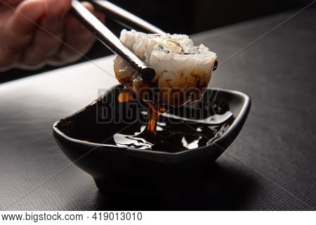 Sushi, Hands Picking Sushi Using Hashi And Dipping In Tare Sauce, Black Background, Selective Focus.