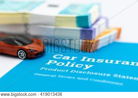 Closeup Shot Of A Small Toy And Car Insurance Papers With Bundles Of Money Defocused In The Backgrou