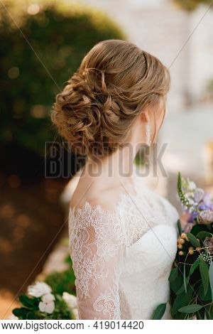 A Bride With A Beautiful Hairstyle In A Lace Dress Stands With A Bouquet And Looks To The Side, Clos