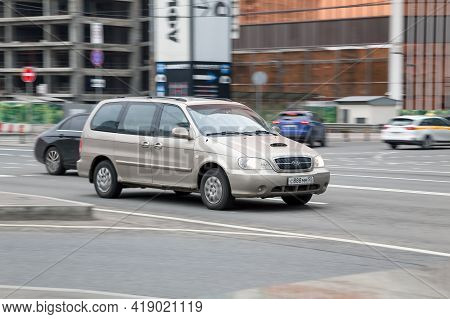 Beige Kia Carnival Minivan Driving Along The Urban Street In City, Side View. Mpv Rides Through The 