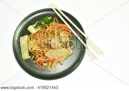 Fried Yakisoba Japanese Noodles Slice Pork And Cabbage With Carrot Eat By Wooden Chopsticks On Plate