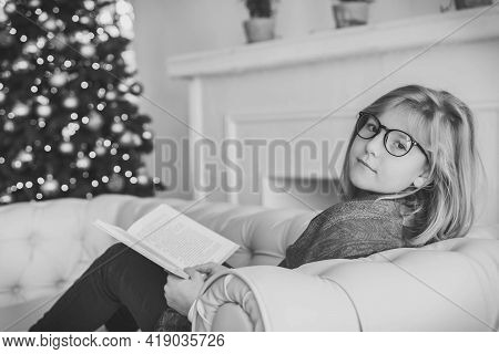 Beautiful Girl Reading A Book On The Sofa Near The Christmas Tree
