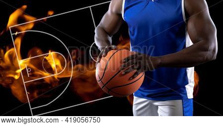 Composition of midsection of basketball player holding basketball over basketball court and fire. sport and competition concept digitally generated image.