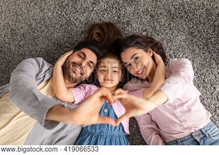 Happy Loving Family. Arab Parents And Liitle Daughter Lying On Floor Carpet And Holding Hands In Hea