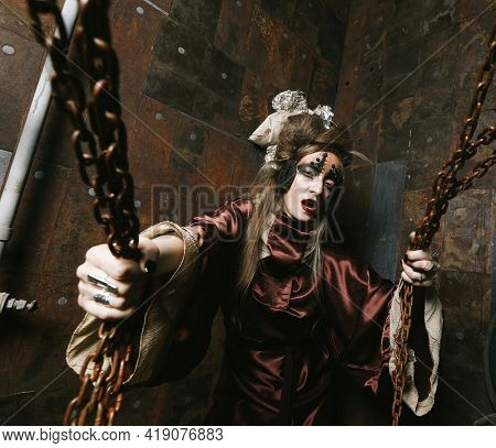 woman with bright makeup in a steampunk scenery holds with her hands for red chains.