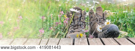 Old Hiking Shoes In A Meadow With Flowers Bloming And A Wooden Terrace