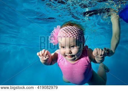 Portrait Of A Charming, Breastfed Baby Who Swims Underwater In A Childrens Pool In A Pink Swimsuit A