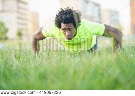 Black Man Doing Push-ups Exercising His Chest On The Grass Of An Urban Park.