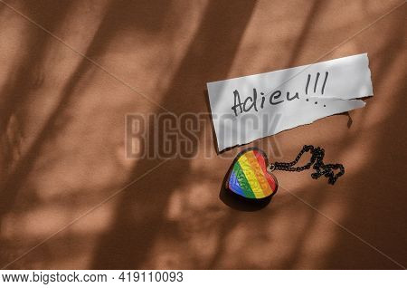 Handwritten Word Adieu On A White Piece Of Paper And A Wooden Amulet In The Shape Of A Heart. Neck C