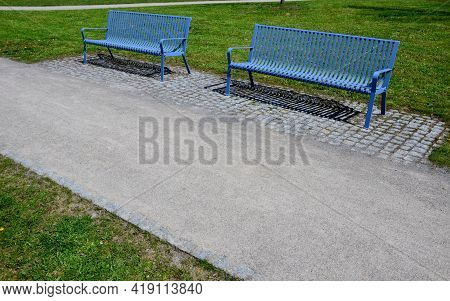 Park Benches In Light Blue Made Of Metal Strips Similar To A Lattice. Trash Can And Beautiful Lawn W
