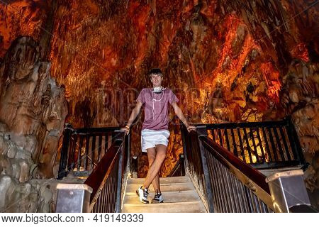 European Man Stands On The Stairs In Damlatas Cave In Alanya (turkey). Tourist In A Natural Undergro
