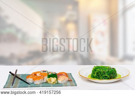 Closeup Of Various Kinds Of Sushi And Chopsticks Served On Green Bamboo Mat And Fresh Chuka Salad Wi