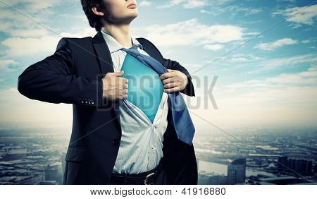 Image of young businessman showing superhero suit underneath his shirt standing against city background