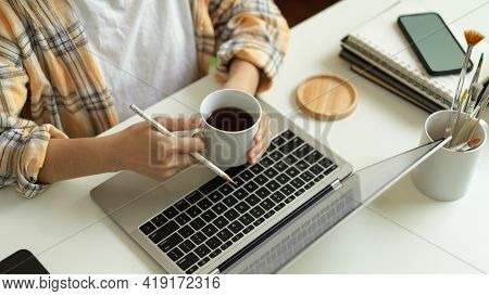 Female Freelancer Hands Holding Coffee Cup While Working With Laptop On Home Office Desk