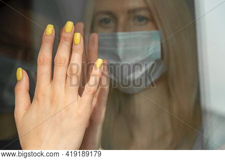 Isolation Of The Coronavirus. An Unhappy Young Blonde Woman In A Mask Touches A Woman's Hand Through