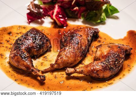 Quail Legs Pan Seared With Madeira Jus, Herbs And Salad On A White Plate