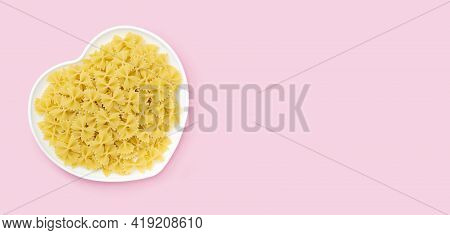 Uncooked Pasta Butterfly Or Bow Tie In A Heart Shape Plate On A Pink Background With Copy Space For 