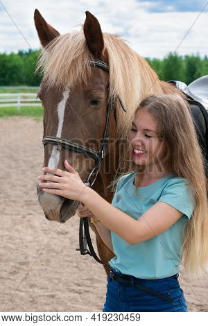 Young Caucasian Woman On Brown Horse Back. Horseback Riding As Hobby In Paddock On Woods. Green Tree