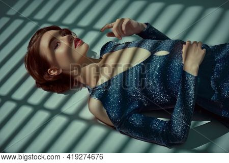 Beautiful girl in evening dress lies on the floor in the shade of sunset. Hair and makeup in the style of the 20s. Art fashion. 