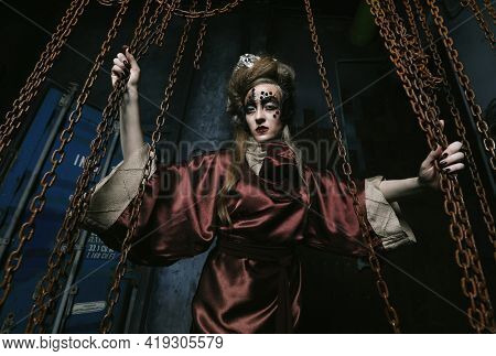 woman with bright makeup in a steampunk scenery holds with her hands for red chains.