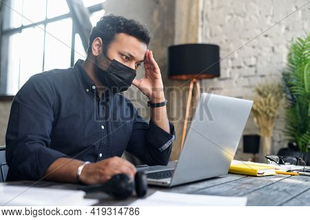 Tired And Worried Hindu Male Employee Wearing Protective Medical Mask Staring At The Laptop Screen, 