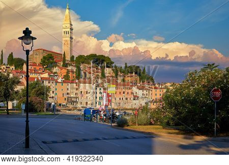 Rovinj, Istria, Croatia. Sunset in medieval old village town of Rovigno, colorful houses and ancient tower during morning sunrise. Picturesque scenic sky with clouds and street lamp by the road.