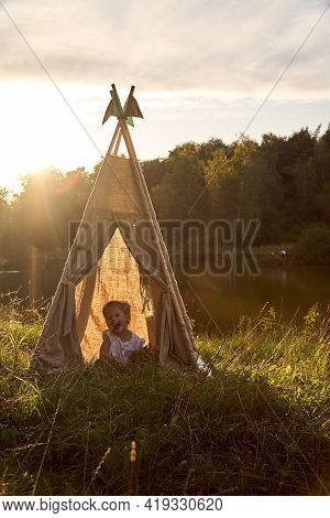 A Little Girl Is Sitting By The Lake. Sunny Akat. Wigwam. Happy Child.