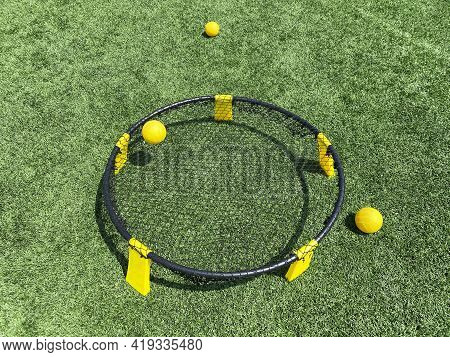 A Yellow And Black Spike Ball Game Is Set Up On A Green Turf Field With Three Balls Ready To Be Used
