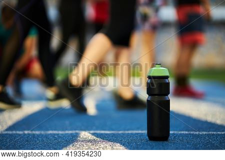 Close Up Black Sports Bottle With Green Cap Stands On A Blue Rubber Treadmill With A White Line. Wat