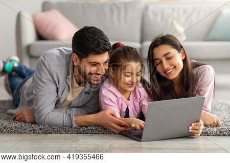 Family Weekend. Cheerful Arab Parents Teaching Their Little Daughter Using Laptop, Spending Time At 