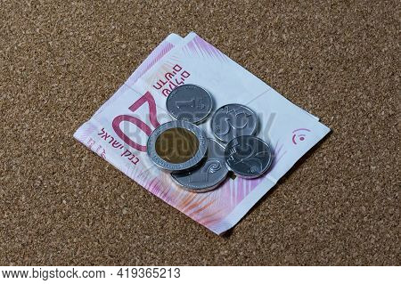 On A Paper Bill Of Twenty Shekels Folded In Half There Is A Pile Of Coins Of Different Denominations