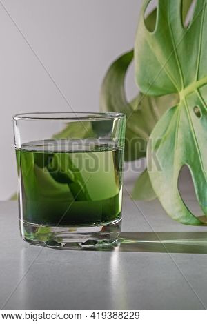 Chlorophyll Extract Is Poured In Pure Water In Glass Against A White Grey Background With Green Leaf