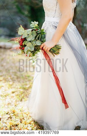A Bride In A Pale Gray Wedding Dress Holds A Bouquet With Red Peonies, Astilba, Roses And Eringium A