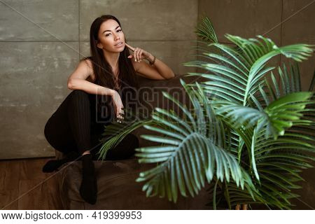 Beautiful Young Woman Closeup Portrait Through Green Leaves Of A Flower On A Gray Wall Background