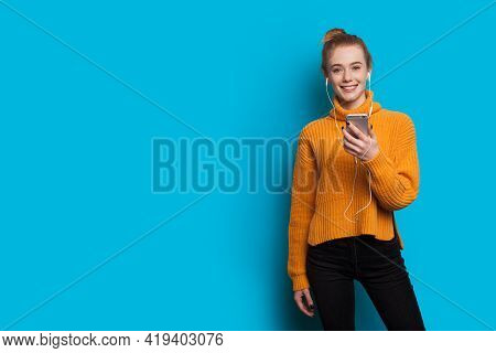 Young Ginger Woman With Freckles Is Listening To Music On A Blue Studio Wall With Free Space Using H