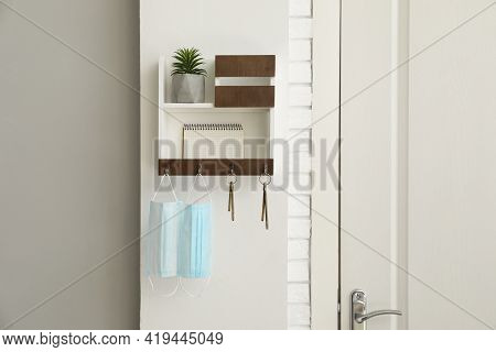 Hanger For Keys With Protective Masks, Houseplant And Notebook On Shelves Near Door In Hallway