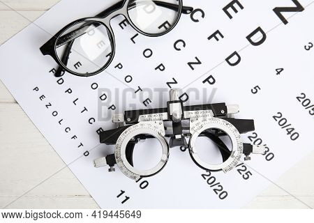 Trial Frame, Eye Chart Test And Glasses On White Wooden Table, Top View. Ophthalmologist Tools